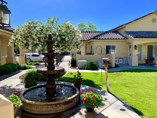 A decorative fountain surrounded by blooming flowers and landscaped grass.