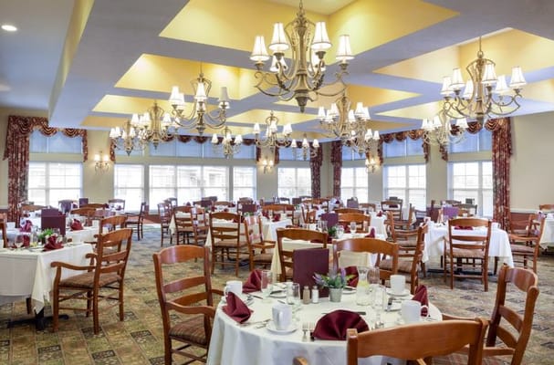 Dining room with tables set for a meal, featuring chandeliers and large windows.