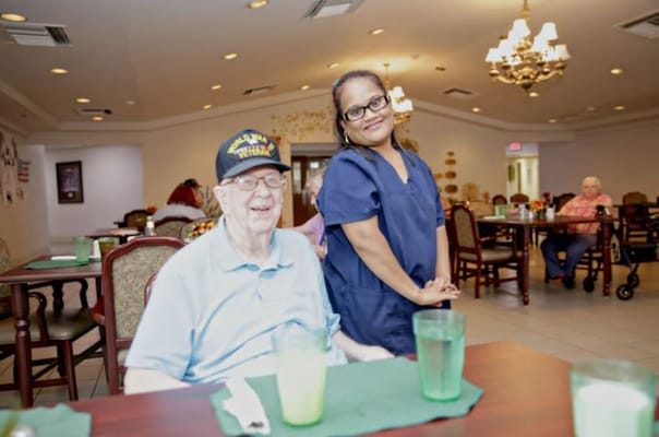Senior resident smiling with staff member in dining area