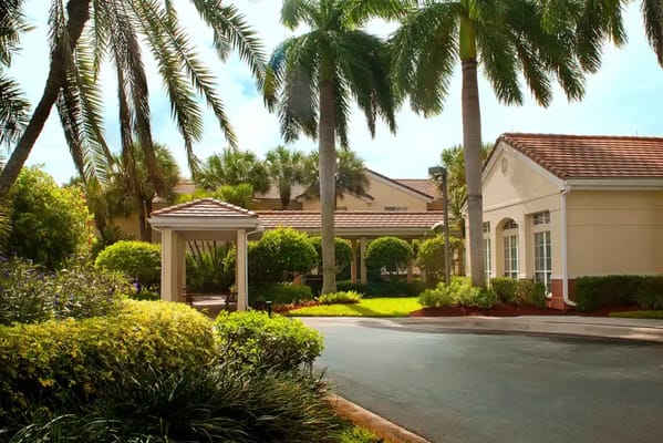 Main entrance surrounded by palm trees and lush landscaping at Barrington Terrace of Boynton Beach.