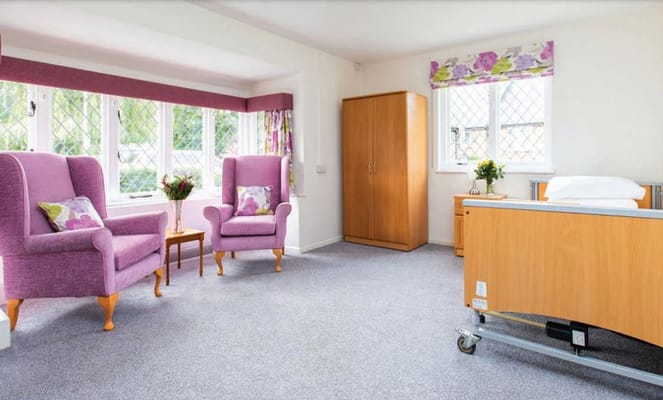 Bright room with two purple armchairs, a bedside table, and a hospital bed.