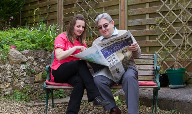 A caregiver and resident enjoying the garden while reading a newspaper