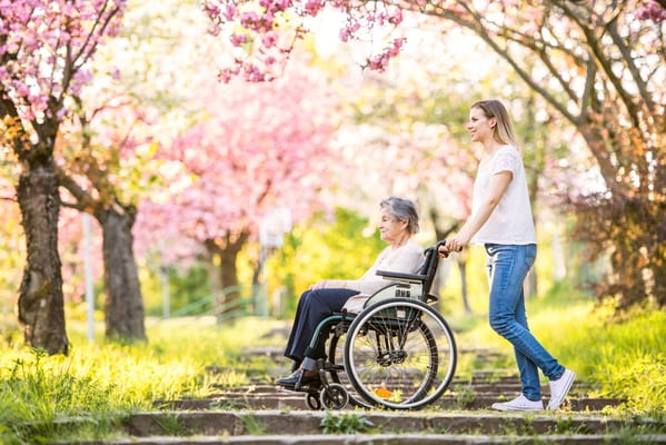 A caregiver pushing a resident in a wheelchair through a blooming garden