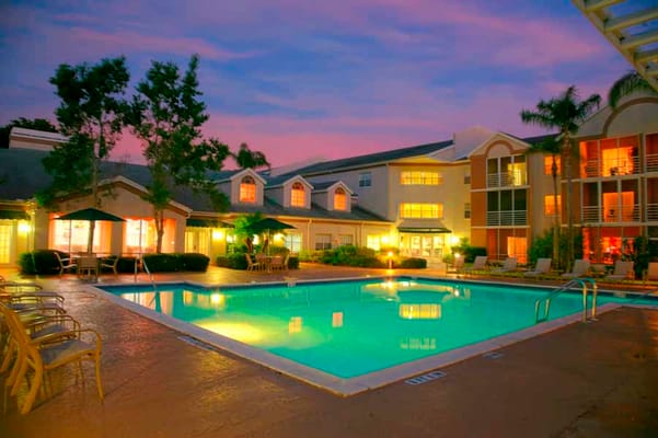 Illuminated pool area surrounded by trees and building at dusk