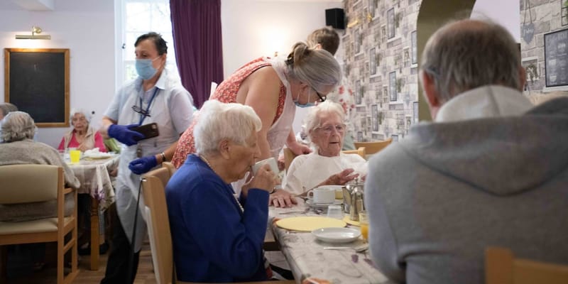 Residents enjoying a meal in the dining room with staff assistance