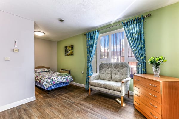 Spacious bedroom with bed, seating area, and window curtains