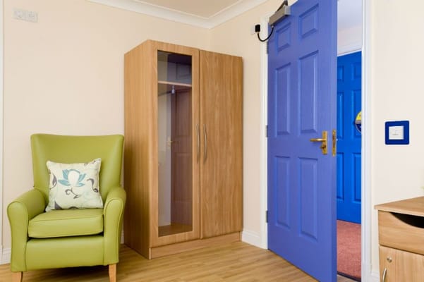 A cozy resident room with a green chair and blue door