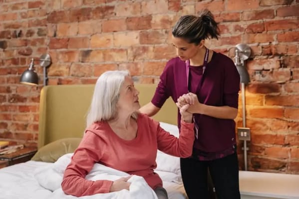 A caregiver assisting a senior woman in a bedroom setting