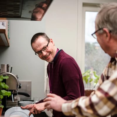 Two men smiling while washing dishes together in a kitchen