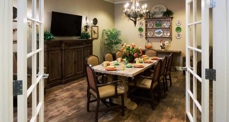 A cozy dining room with a long table set for a meal, featuring colorful plates and a floral centerpiece.
