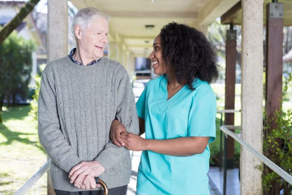 A resident and caregiver smiling outdoors in a walkway