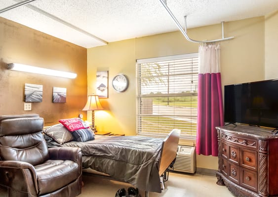 Colorful room with a bed, armchair, and TV in Jourdanton Nursing and Rehab.