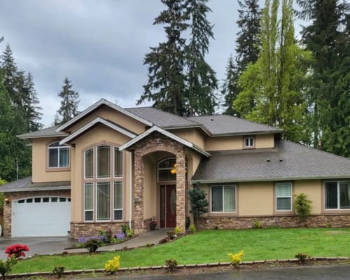 Front view of a beige house with stone accents amidst trees