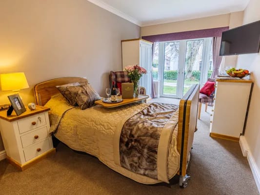 A neatly arranged bedroom with a bed, nightstand, and a view of the garden
