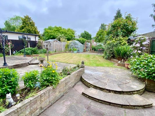 A well-maintained garden with a lawn, flower beds, and greenhouse.