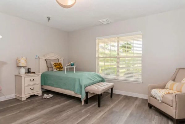 A well-lit, cozy bedroom with a bed, nightstand, and seating area.