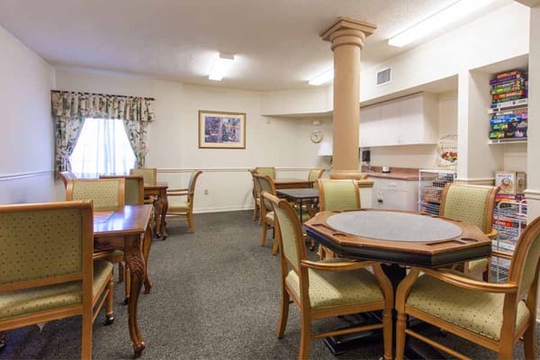 Cozy dining area with wooden tables and chairs, featuring a light-colored wall and window curtains.