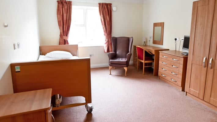 A well-furnished room with a bed, armchair, desk, and wardrobe.