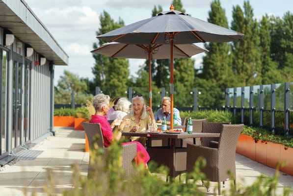 Residents enjoying refreshments under an umbrella on a patio