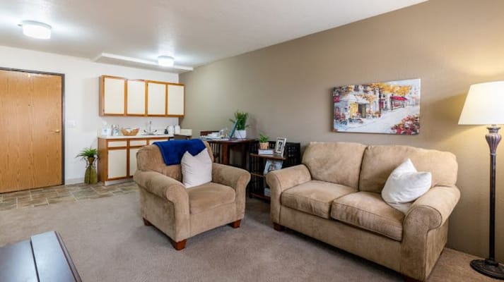 A cozy living room with beige sofas and a kitchenette.