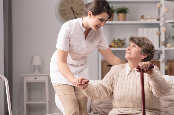 Caregiver helping an elderly woman with a cane in a cozy living space.