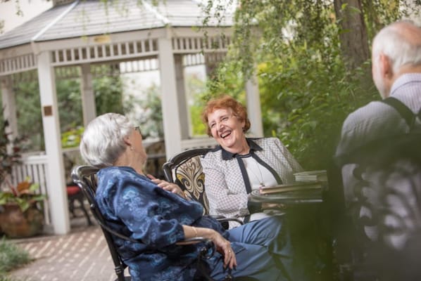 Two seniors laughing and enjoying a conversation in a garden setting.