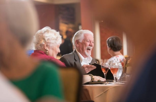 Seniors laughing and enjoying drinks during a meal.