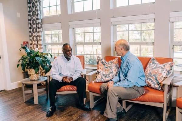 Two residents conversing in a common area with large windows