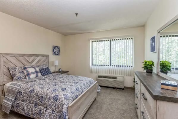 A neatly arranged bedroom with a bed, dresser, and natural light.