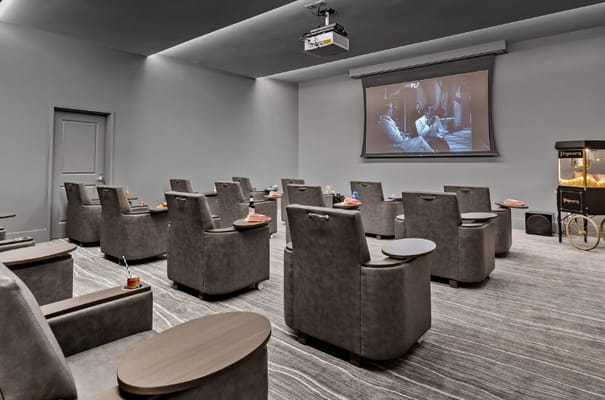 An indoor theater room with seating and a large screen showing a movie.