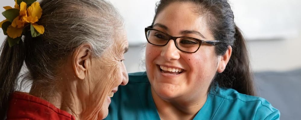 A caregiver and a resident smiling at each other.
