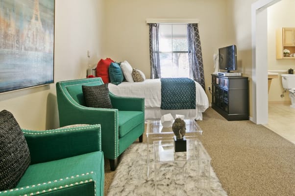 Comfy living area with two green chairs, a bed, and a TV