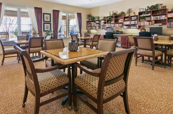A bright common area featuring tables, chairs, and computers.