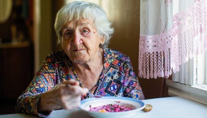 Senior woman sitting at a table, eating a colorful meal.