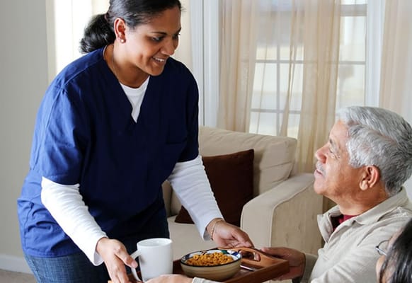 Caregiver serving food to senior resident in a cozy room