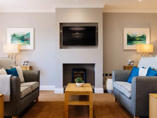 Lounge area with two armchairs, a coffee table, and a TV mounted on the wall