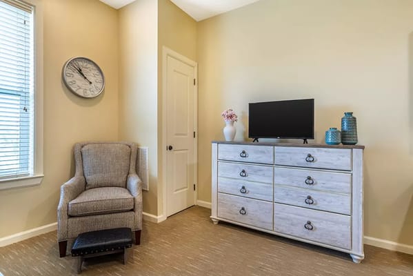 A cozy living room featuring a chair, dresser, and television.