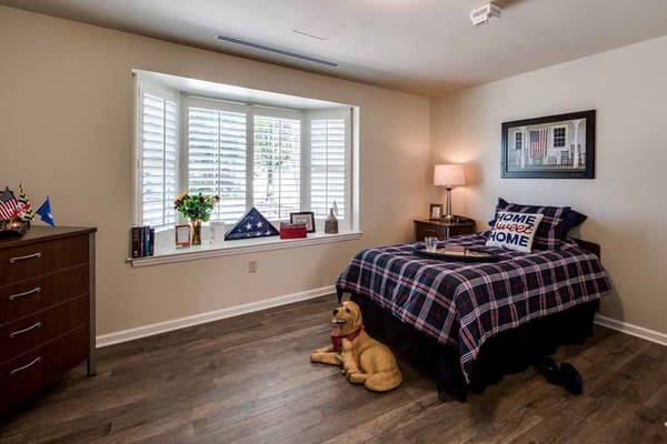 A cozy senior bedroom featuring a bed with plaid bedding, a dresser, and a dog statue.