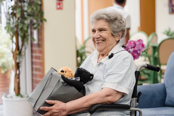 Smiling woman in wheelchair holding stuffed animals and a gift bag
