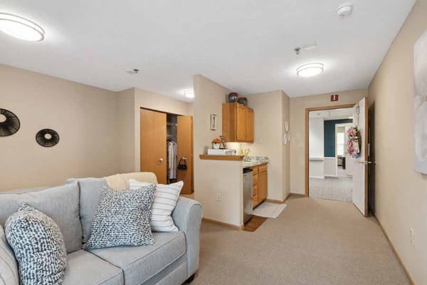 Comfortable living space with a couch and kitchenette in senior living facility.