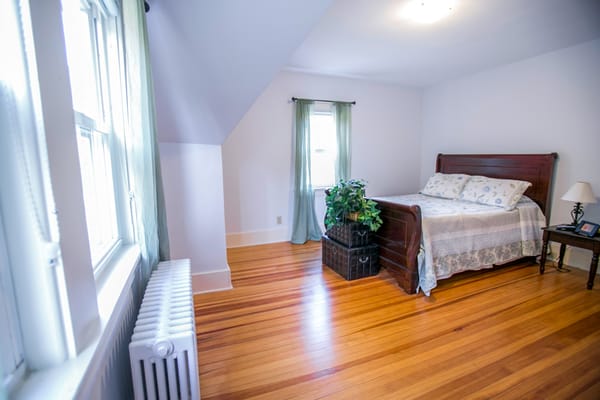 A cozy bedroom featuring a bed, nightstand, and window with green curtains.