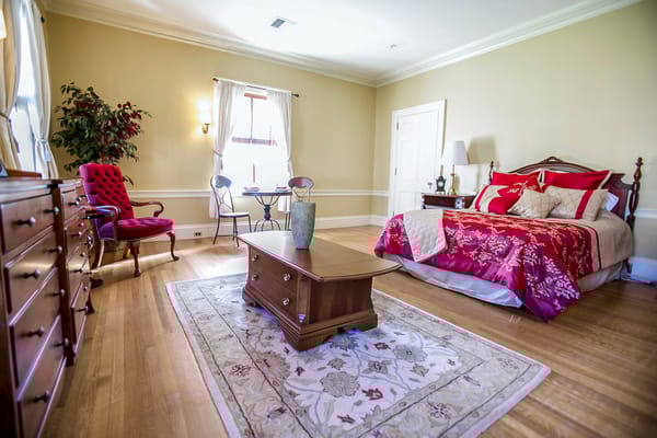 A well-decorated bedroom featuring a bed, dresser, and seating area.