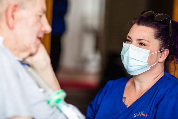 Caregiver wearing a mask speaks with a senior resident.