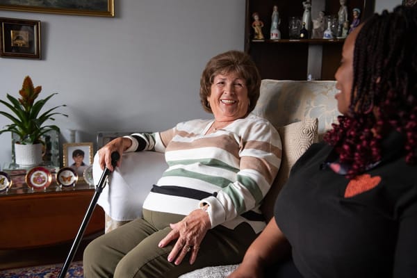 A senior woman smiling while sitting next to a caregiver