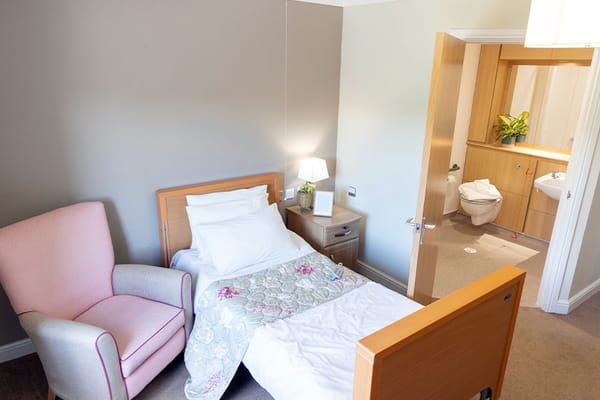 Cozy bedroom with a bed, pink armchair, and an ensuite bathroom