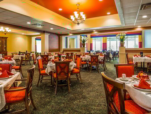 Brightly lit dining room with orange accents and neatly set tables.