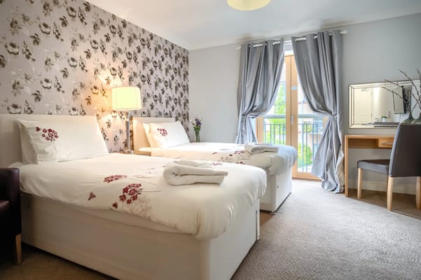 A neatly arranged bedroom with two beds, a lamp, and a view of a balcony.