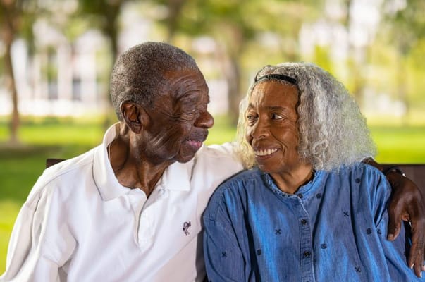 An elderly couple sitting closely together, smiling at each other.