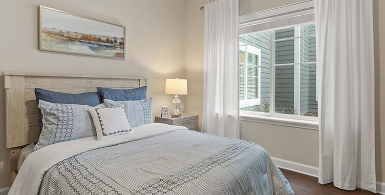 A comfortable bedroom with a bed, decorative pillows, lamp, and window.