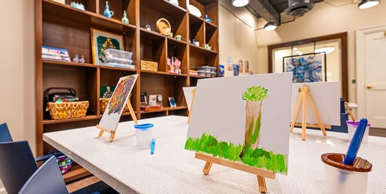 A spacious art room with easels displaying children's paintings and a shelf filled with art supplies.